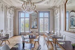 Un espace repas agrémenté de détails décoratifs au plafond, de grandes fenêtres et d’un lustre.