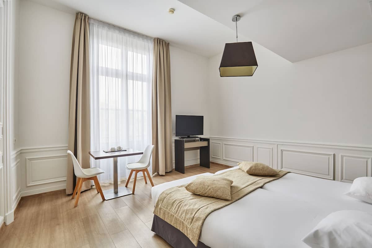 Ein Hotelzimmer mit einem Bett, einem Schreibtisch mit Stuhl, einem Fernseher und einem Fenster mit Vorhängen.