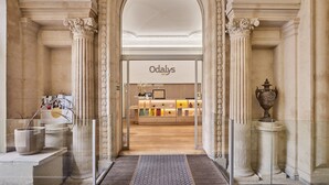 Une entrée imposante, ornée de colonnes richement décorées, mène à un magasin appelé « Odalys ».