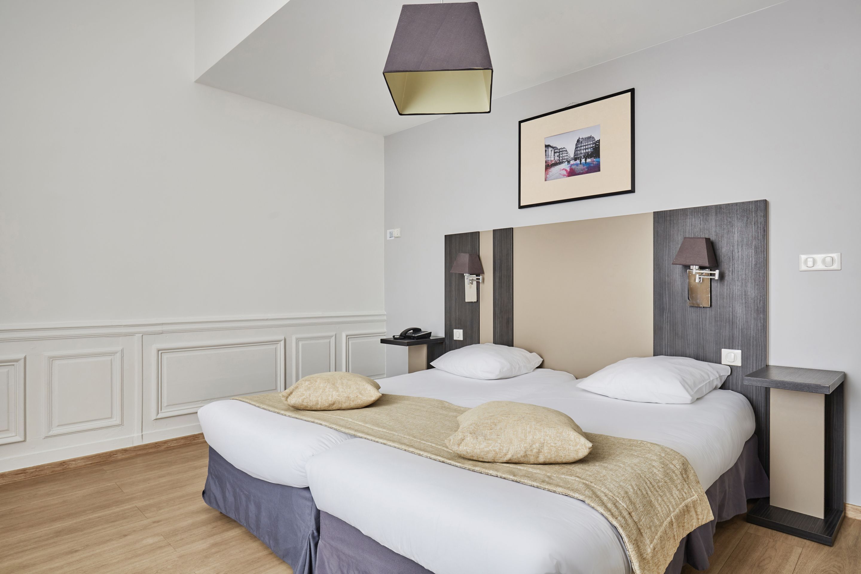 A modern hotel room with a large bed, bedside tables, a hanging lamp, and a framed picture on the wall.