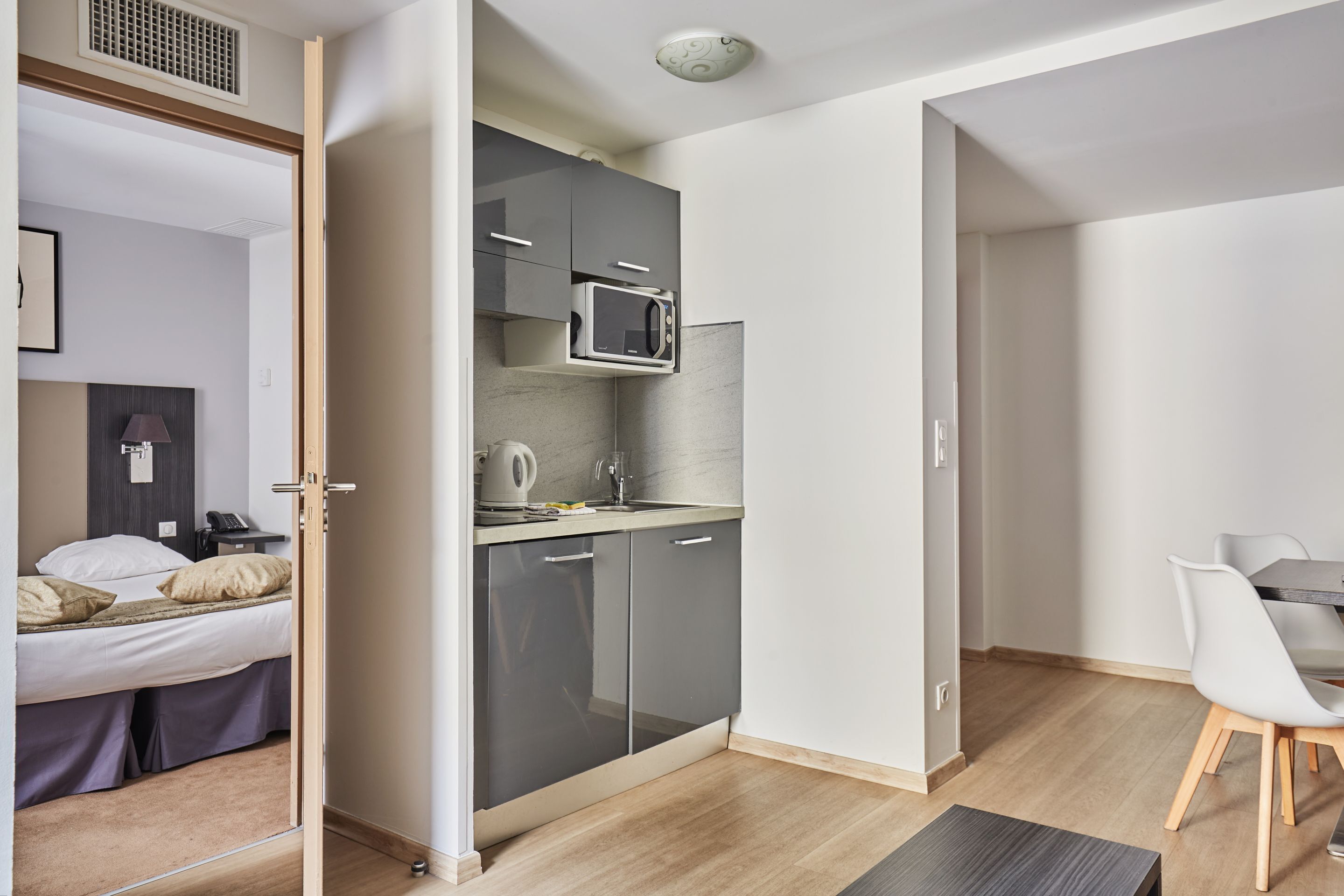 A compact hotel room with a kitchenette, a bed, and a dining area.
