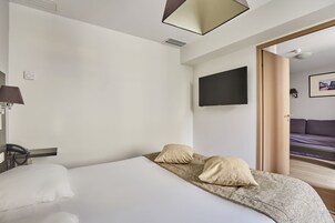 Una habitación de hotel con una cama, un televisor de pantalla plana montado en la pared, un teléfono y una puerta que da a otra habitación.