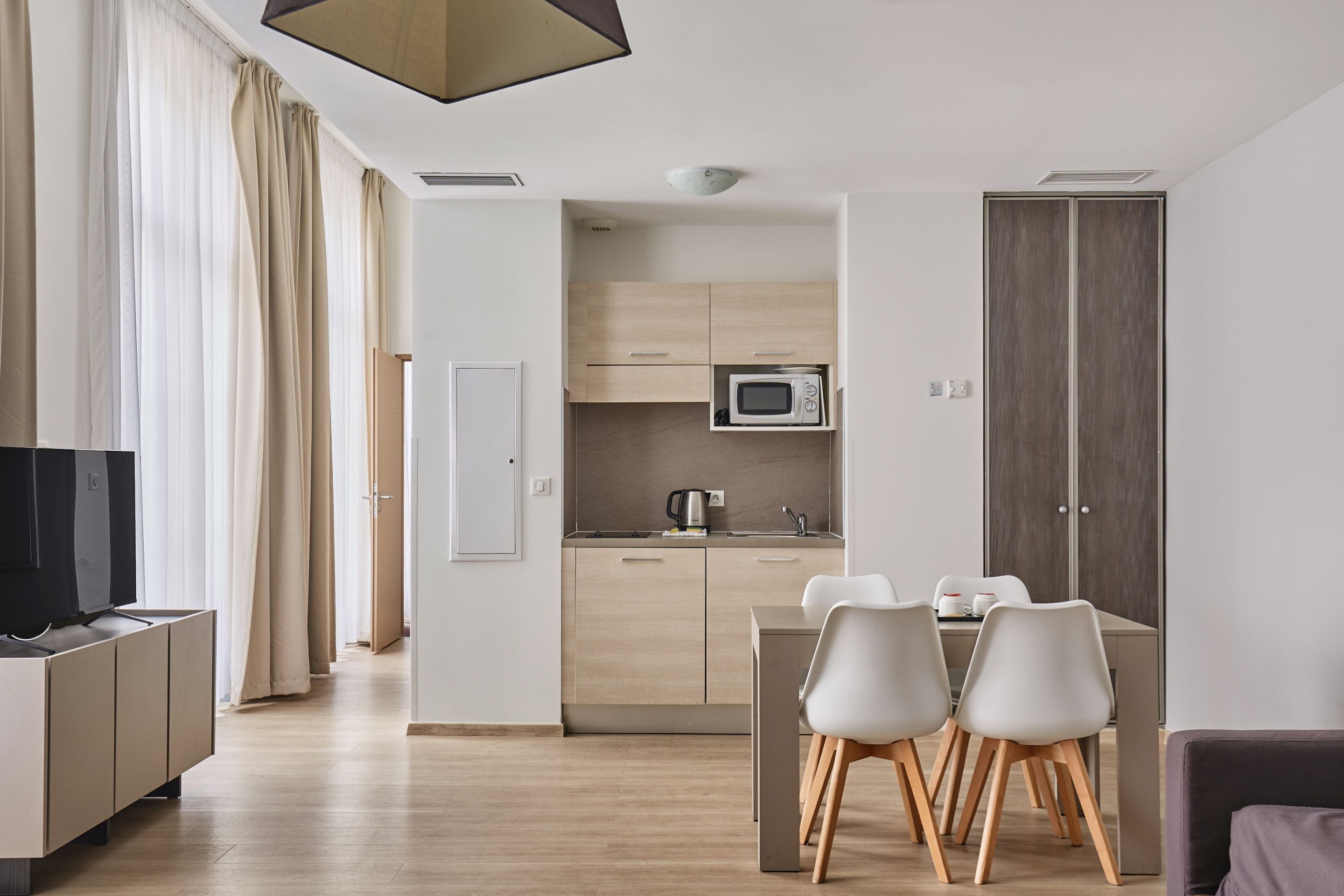 Ein modernes Wohnzimmer mit Flachbildfernseher, ein Essbereich mit Tisch und Stühlen, eine Küche mit Mikrowelle und ein Kleiderschrank.