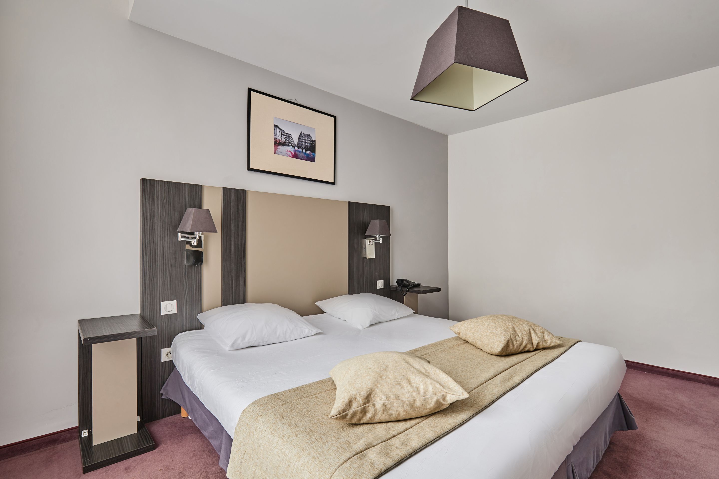 Quarto de hotel moderno com uma cama grande, mesas de cabeceira, uma luminária de parede e um quadro emoldurado na parede.