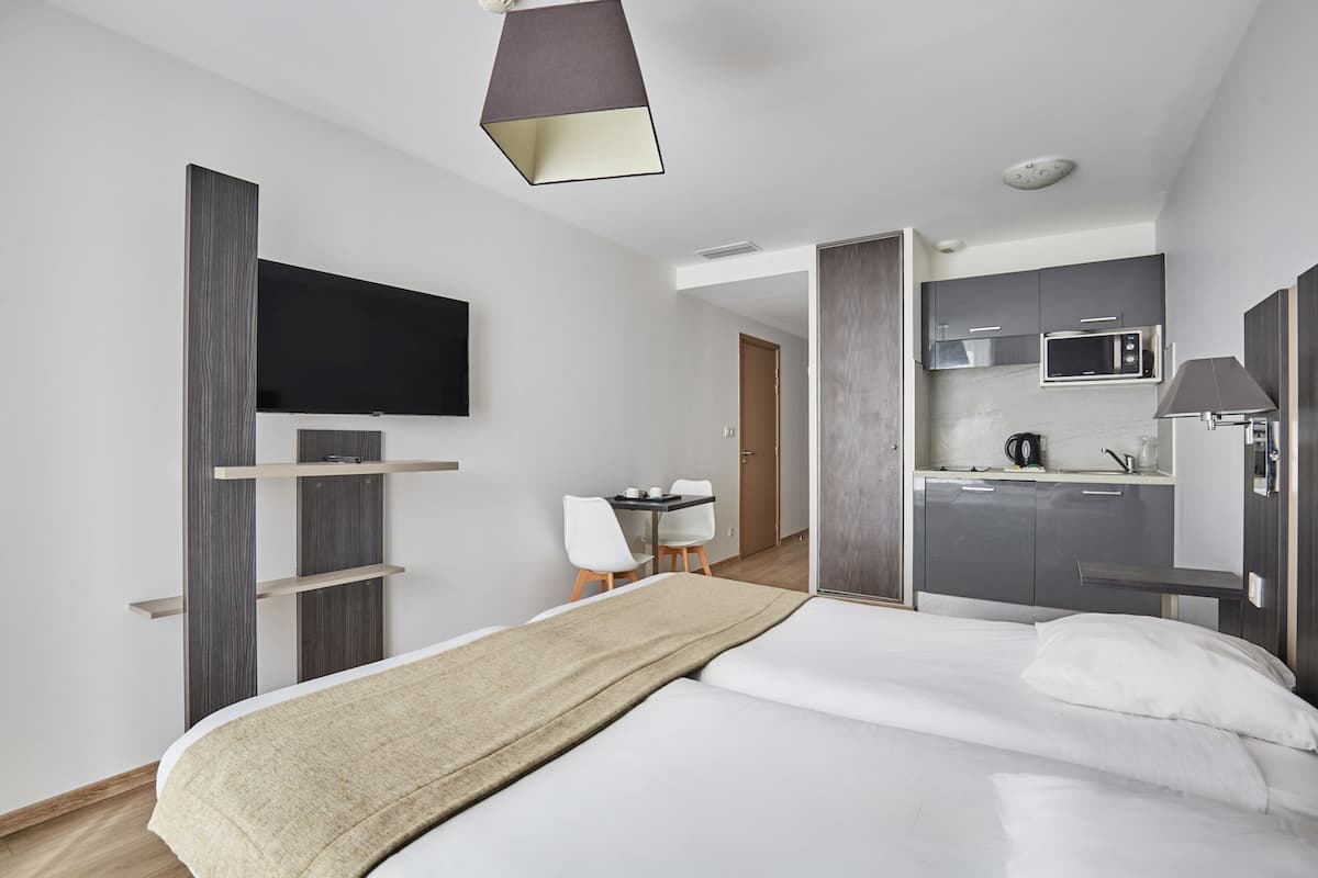 Ein modernes Hotelzimmer mit Bett, Schreibtisch, Stuhl, Fernseher und einer Küchenzeile.