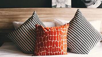 A bed with a wooden headboard, three pillows with different patterns, and a framed picture on the wall.