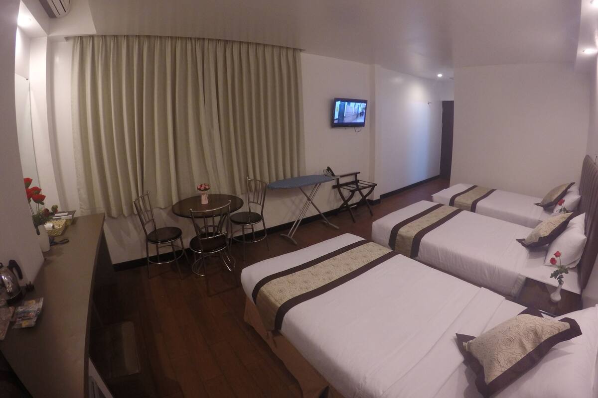 Ein Hotelzimmer mit zwei Betten, einem Schreibtisch, einem Stuhl, einem Fernseher und einem Esstisch.