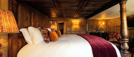 A large bed with a wooden headboard, a red throw blanket, and multiple pillows.