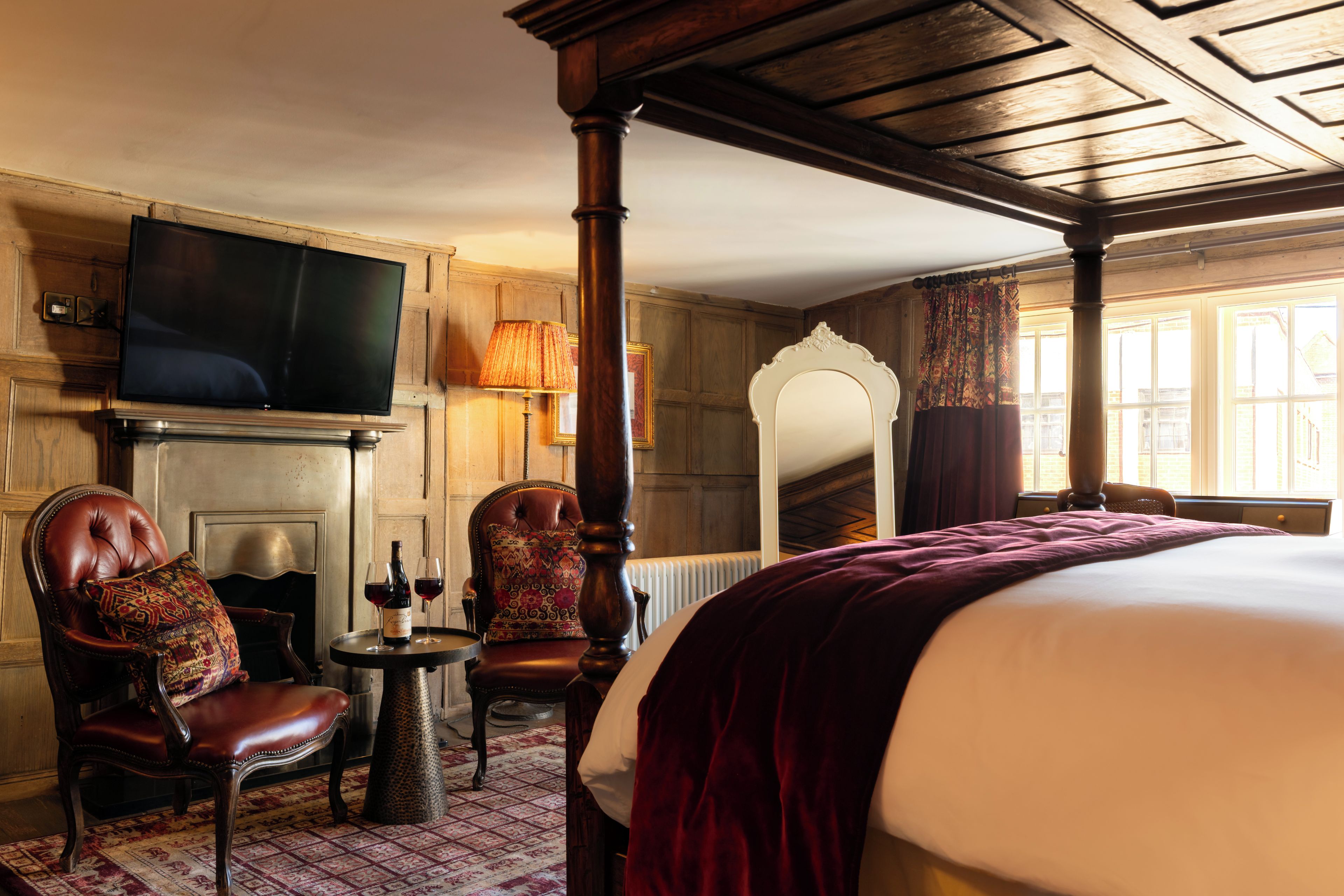 Habitación de hotel con una cama, un televisor montado en la pared, chimenea, espejo y ventana con cortinas.