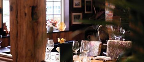 Una mesa de restaurante dispuesta con copas de vino, un menú y un florero con flores.