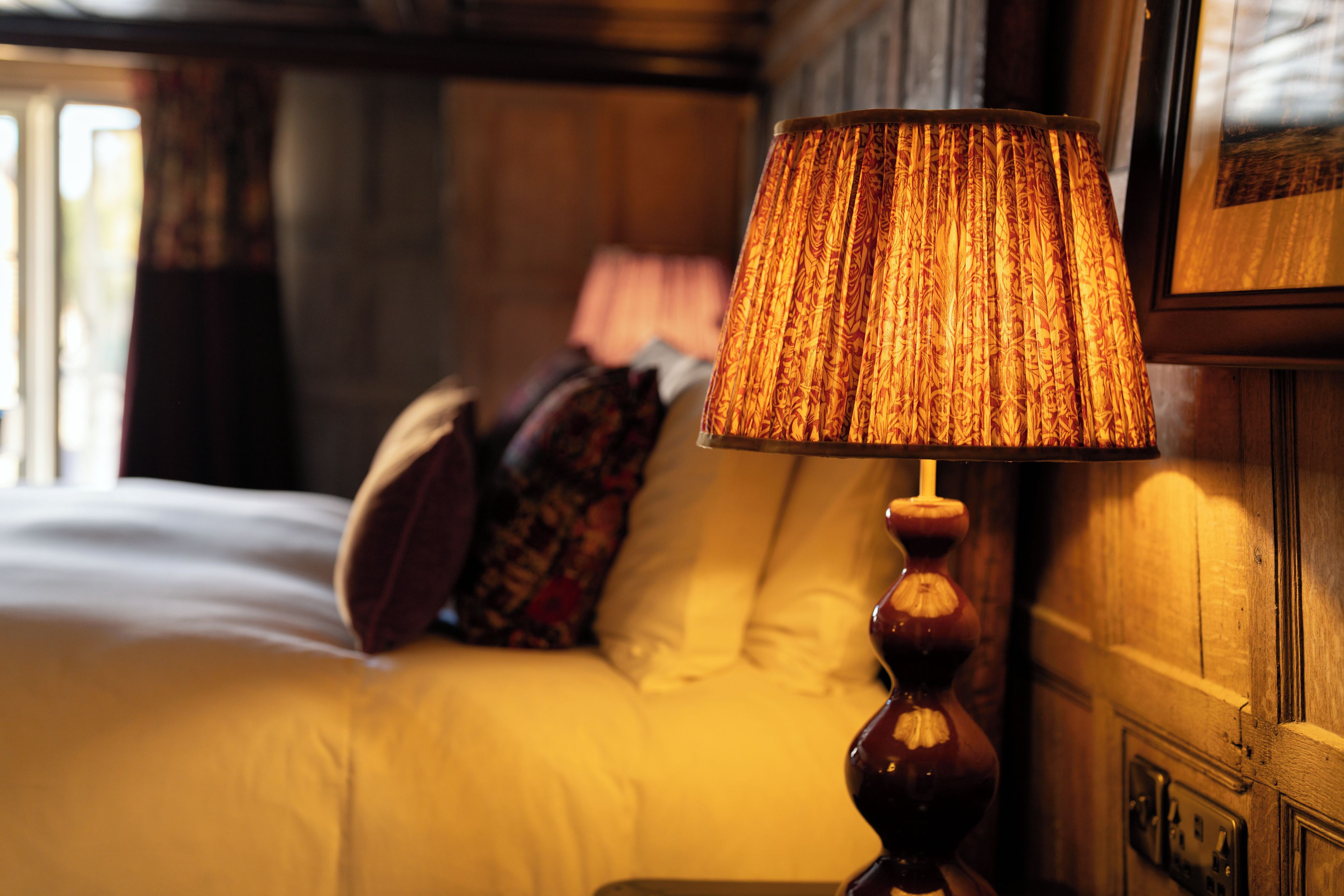 A bed with a headboard, a bedside table, and a lamp with a patterned lampshade.