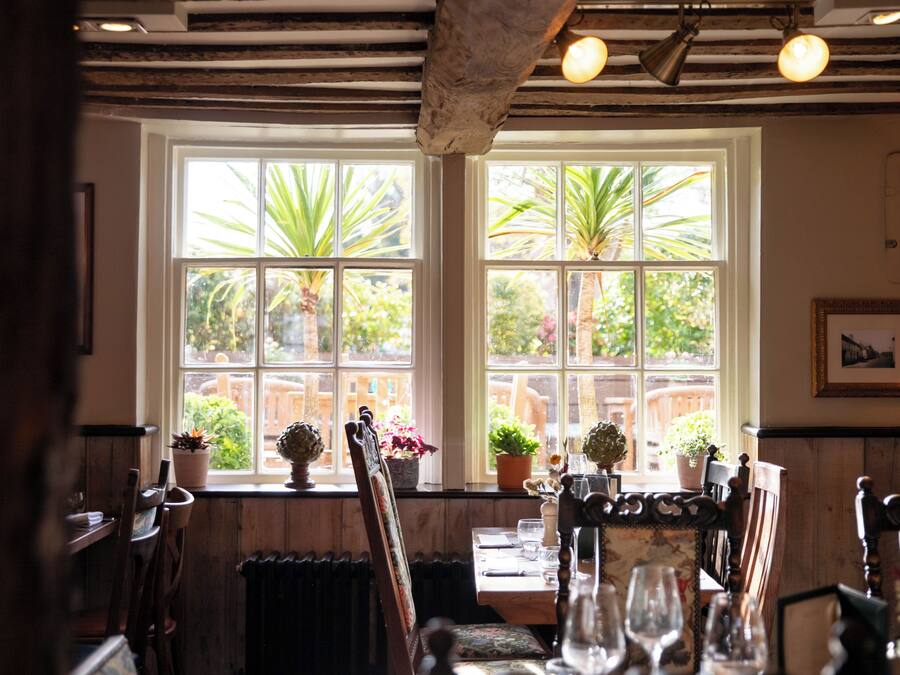 A dining area with a table set for two, wooden chairs, and potted plants on the windowsill.