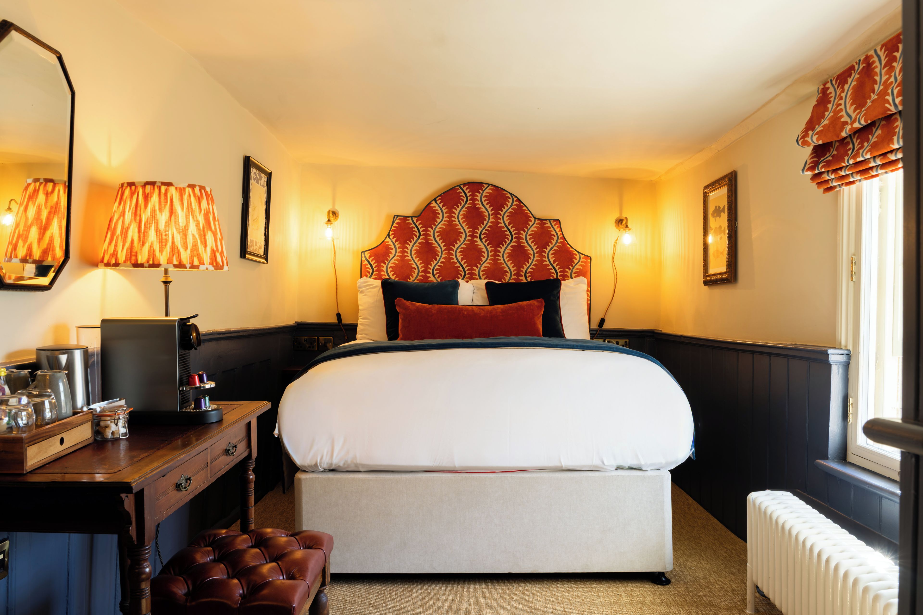 Una habitación de hotel con una cama, mesitas de noche, un escritorio y un radiador.
