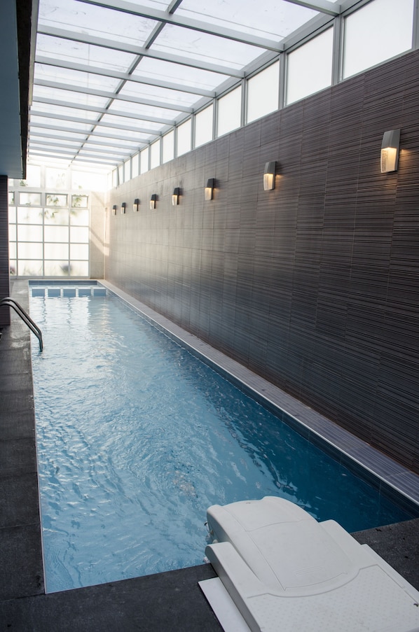 Una piscina interior con pared de azulejos y techo de cristal.