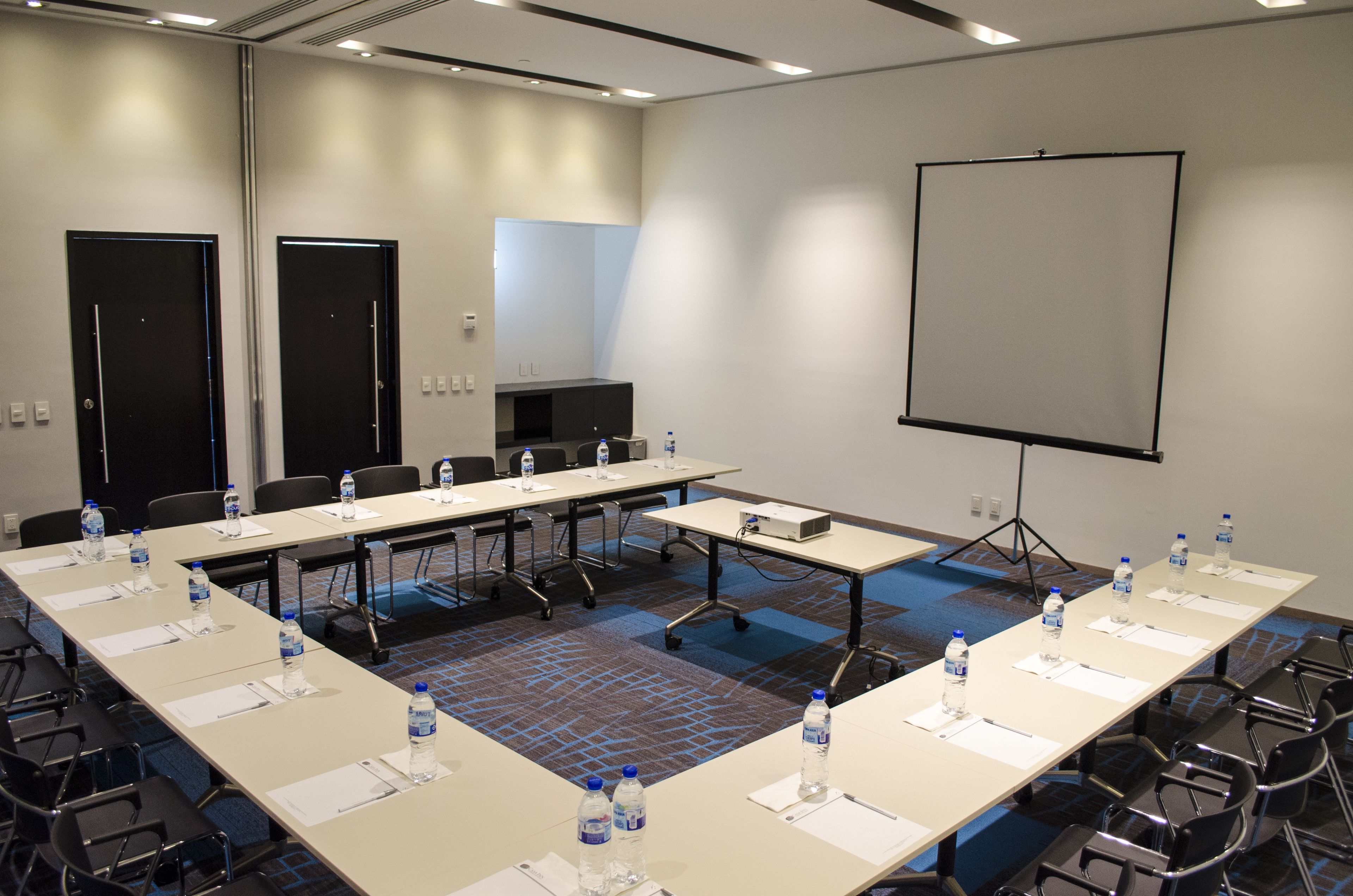 A conference room with a long table, chairs, water bottles, a projector, and a screen.