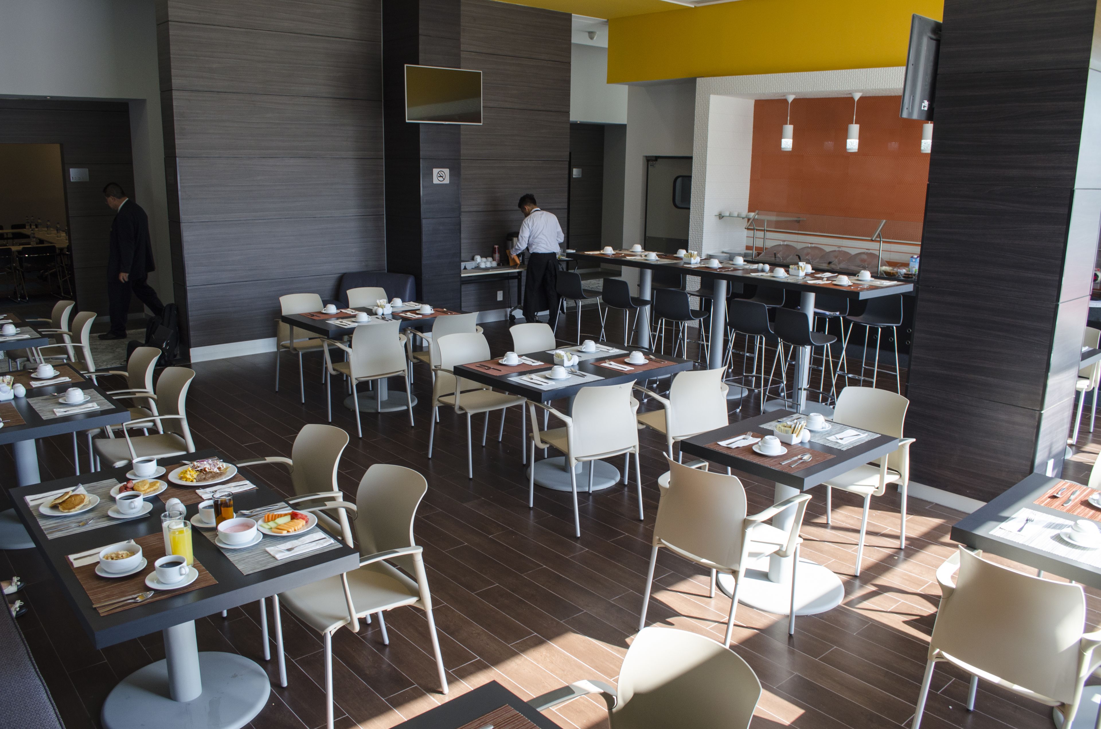Un comedor moderno con varias mesas y sillas, un chef preparando comida, y un diseño limpio y contemporáneo.