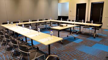 A conference room with long tables, chairs, water bottles, and a projector.