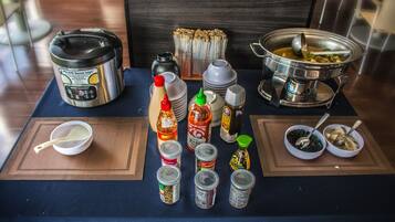 A table with various condiments, a rice cooker, and a soup pot, suggesting a self-service dining setup.