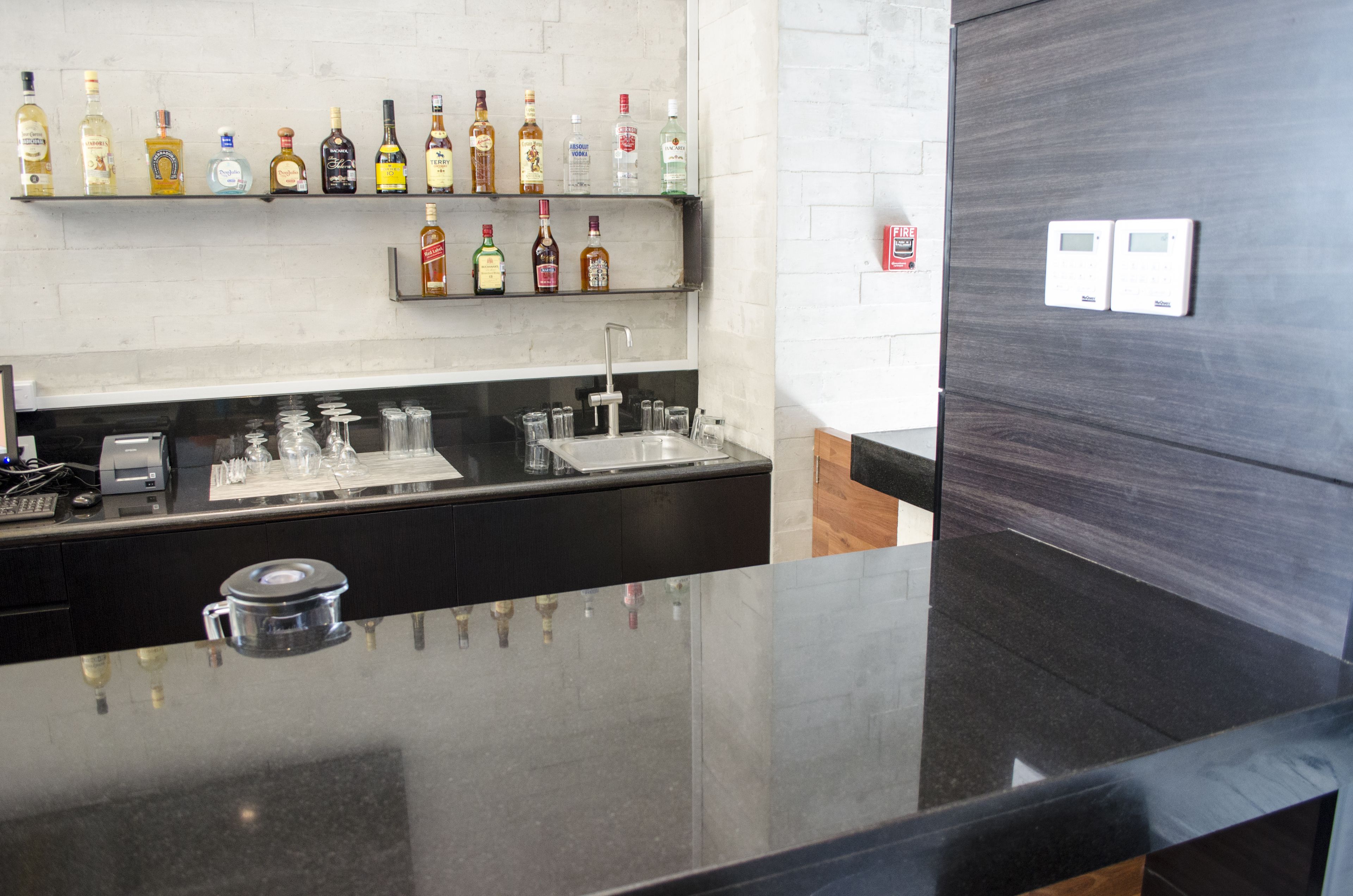 Una zona de bar con encimera de granito pulido, diversas botellas de licor en estantes y un grifo moderno.