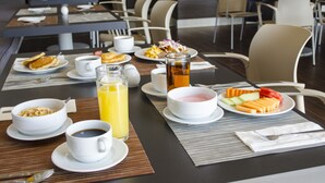 A breakfast setting with various dishes, beverages, and a dining area with chairs and tables. - Hotel Casa Inn Galerias (Celaya)