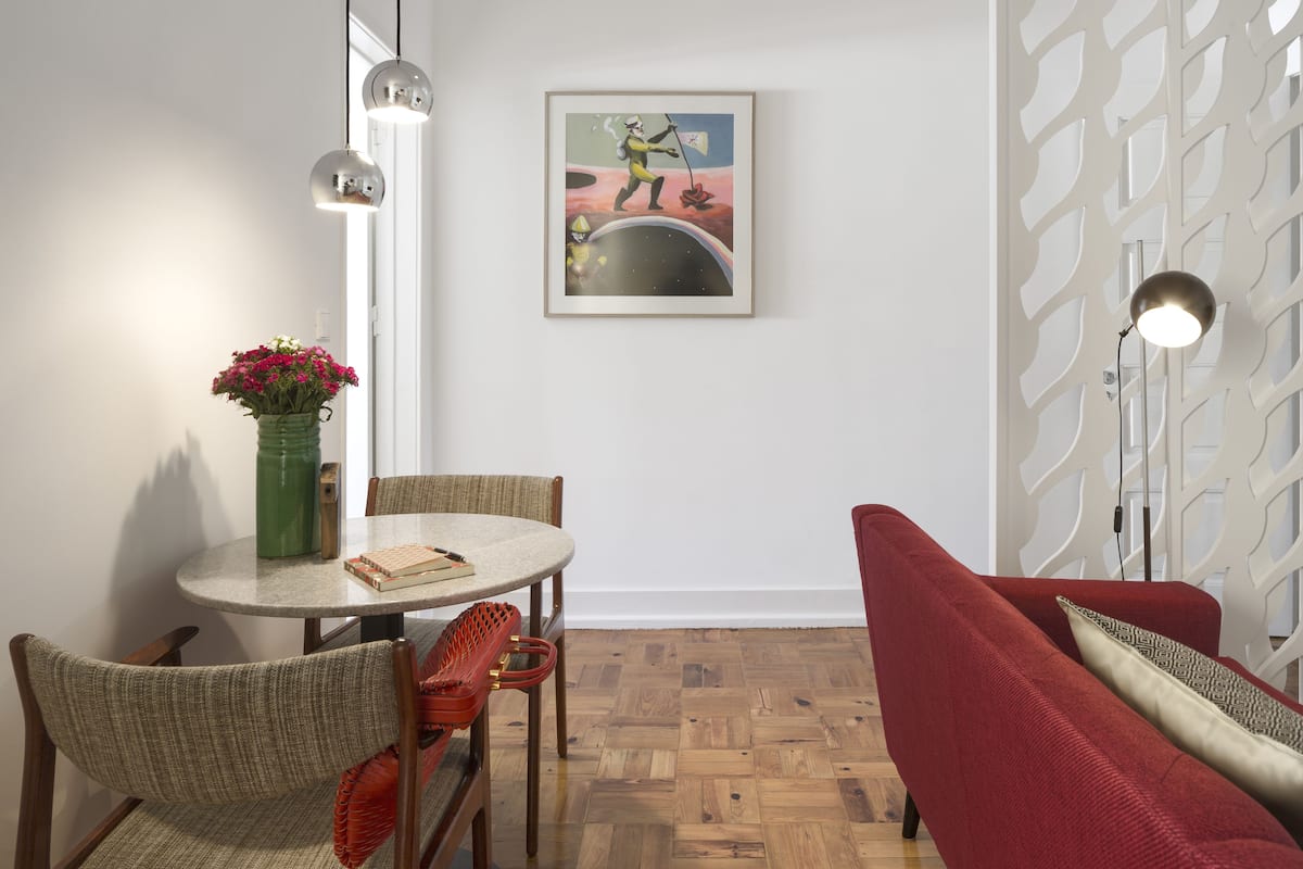 A dining area with a round table, chairs, a vase with flowers, a framed artwork, and a patterned partition.
