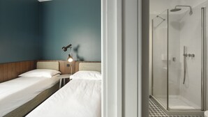 Une chambre d’hôtel avec deux lits, une table de chevet, une lampe et un espace douche.