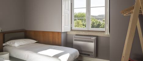 A bedroom with a bed, a window with an open door, a radiator, and a wooden ladder.