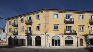 A yellow building with multiple windows and balconies, featuring a sign for 'SEGUROS' and a blue directional sign.