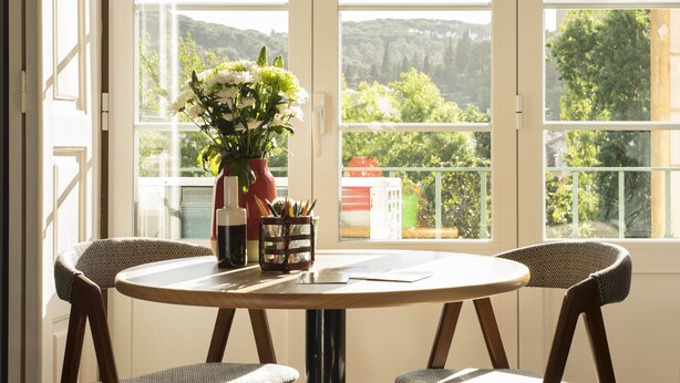 A round table with four chairs, a vase with flowers, and a pen holder with pencils.