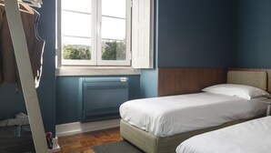 A bedroom with two beds, a window, a radiator, and a suitcase on the floor.