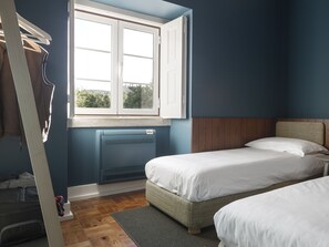 A bedroom with two beds, a window, a radiator, and a suitcase on the floor.