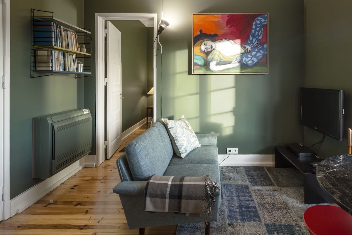 A living room with a grey sofa, a red chair, a black TV, and a painting on the wall.