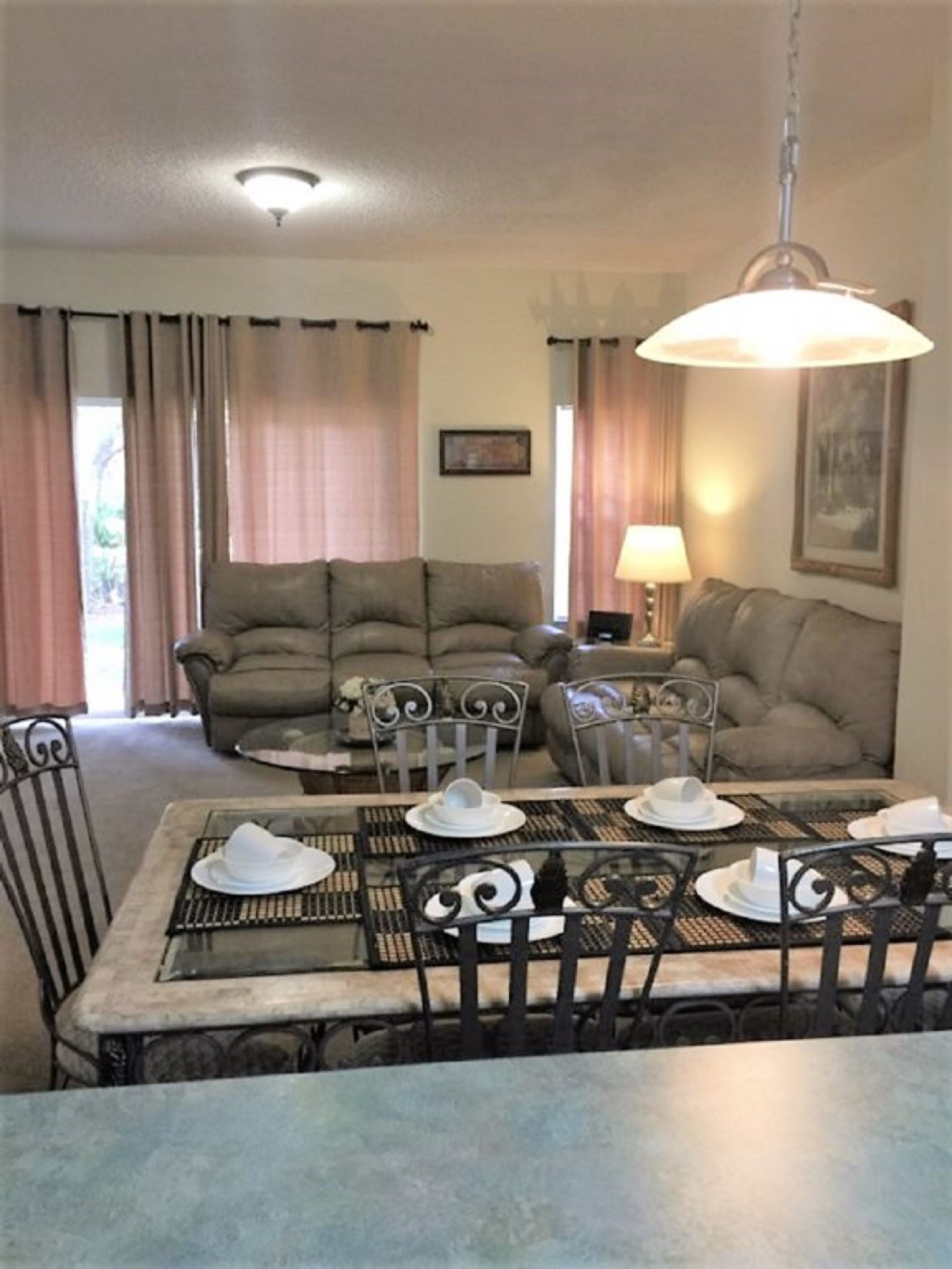 A dining area with a table set for four, two sofas, and a lamp.