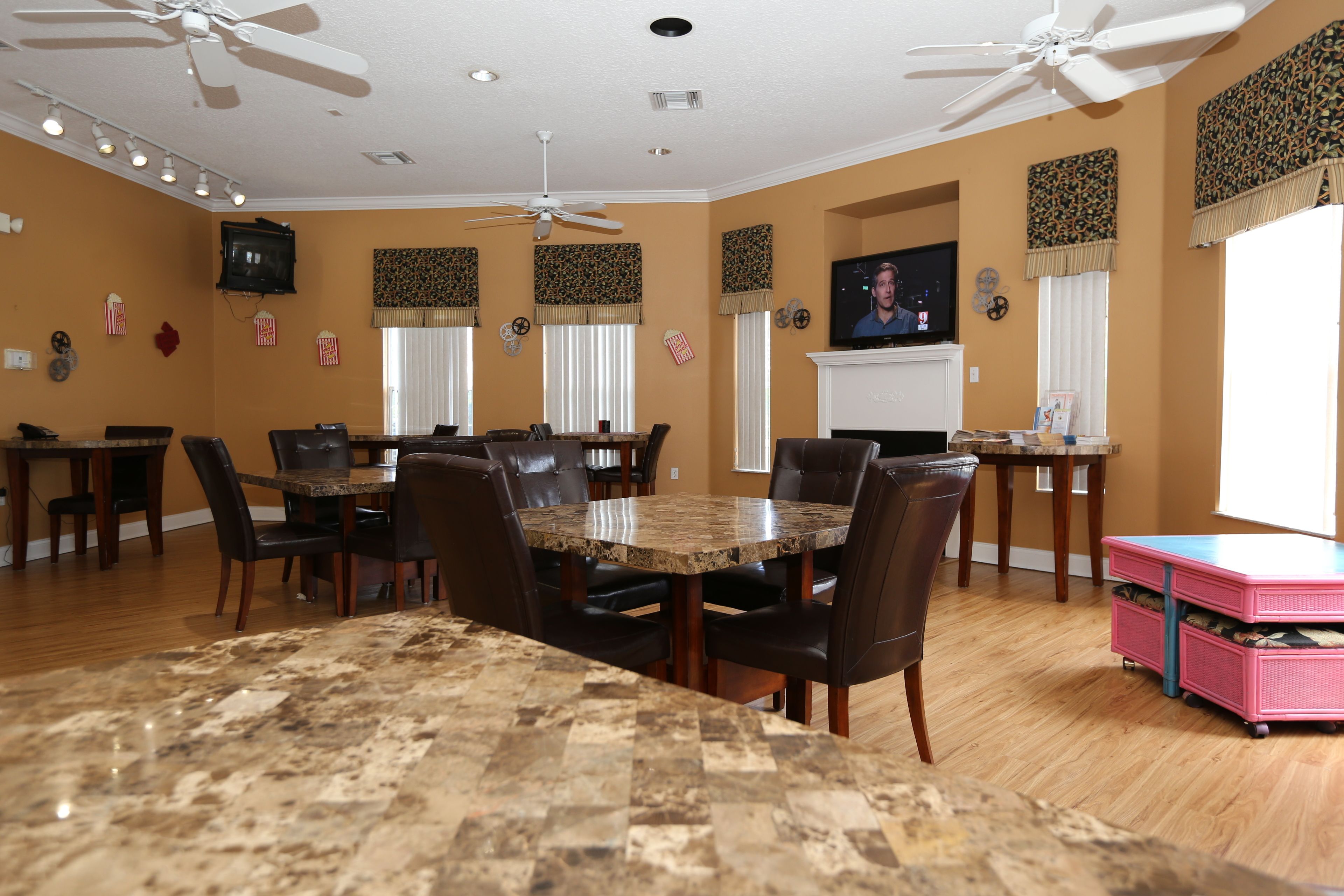 A dining area with a large granite table, leather chairs, ceiling fans, and a television mounted on the wall.
