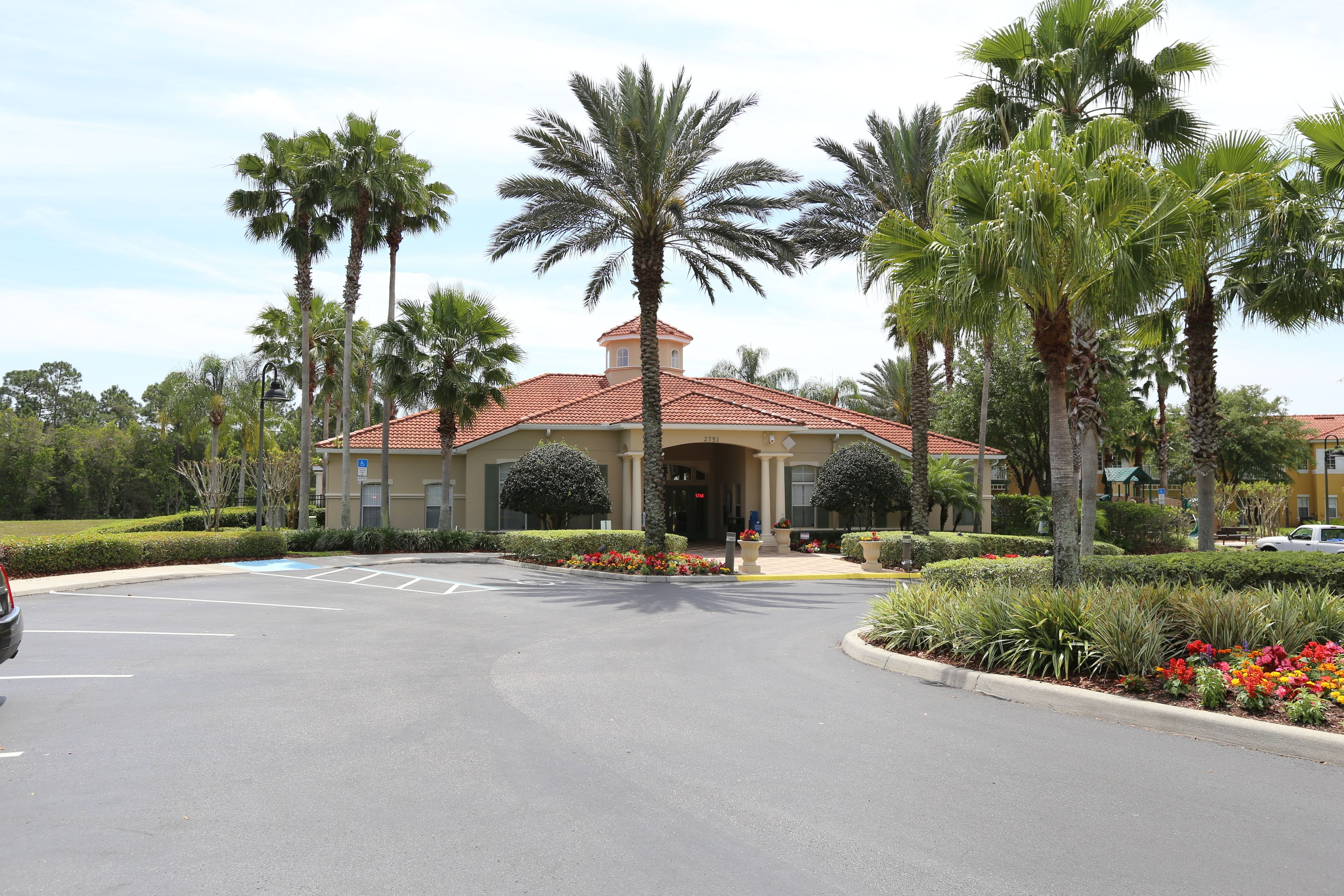 A hotel entrance with a red-tiled roof, palm trees, and a parking lot.