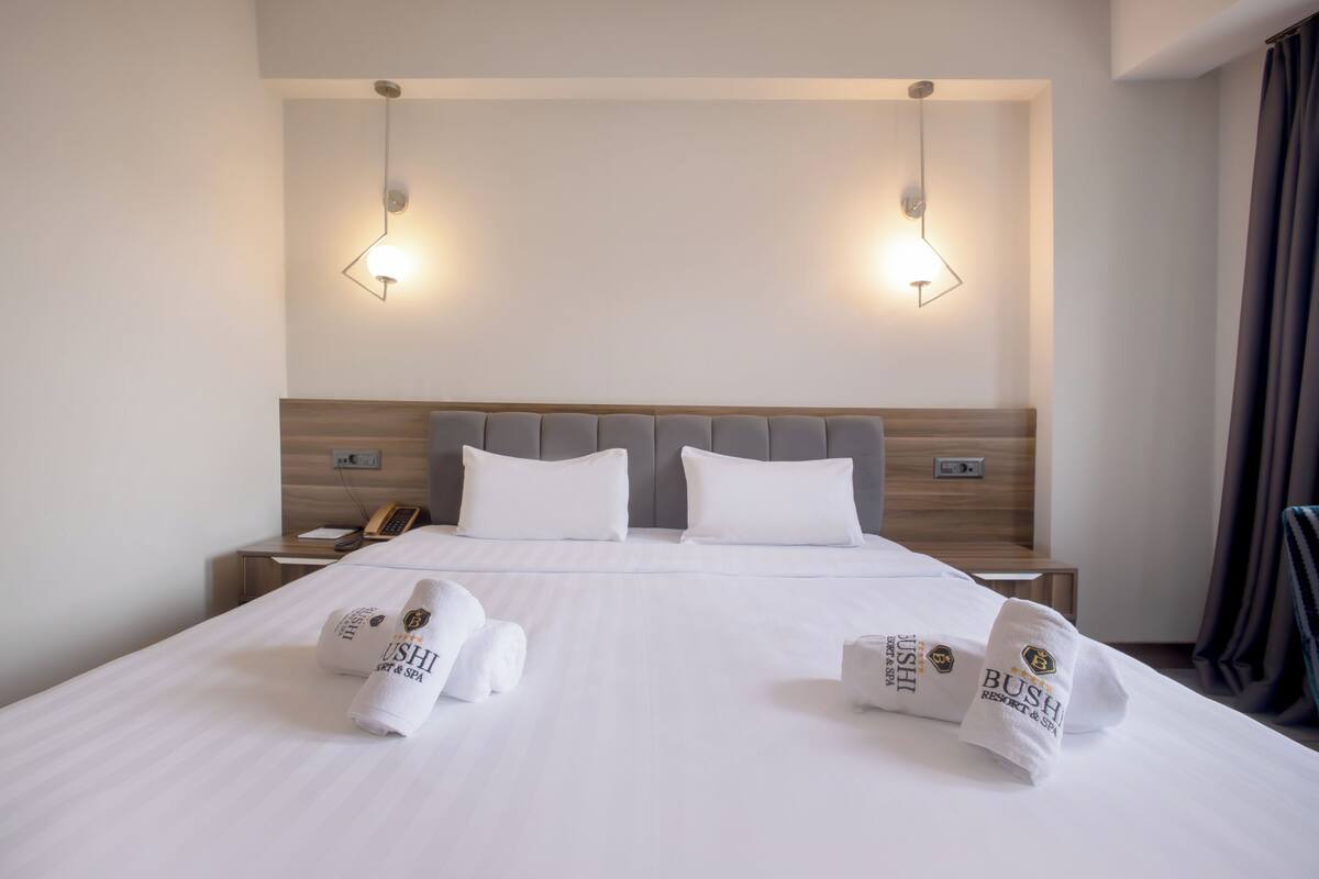 A hotel room with a large bed, two bedside tables, a wooden headboard, and two wall-mounted lights.