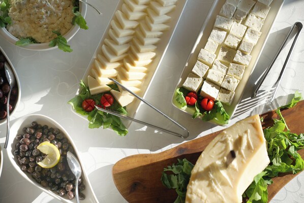 Buffet com diversos alimentos, incluindo uma saladeira, queijo e uma tábua de madeira com um pedaço grande de queijo.