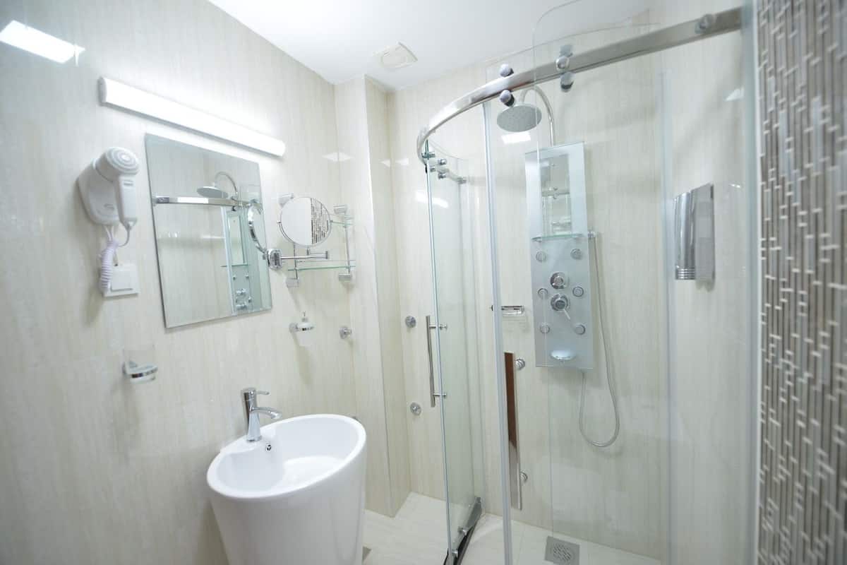 A modern bathroom with a glass-enclosed shower, a white sink, and a mirror with a round mirror above it.