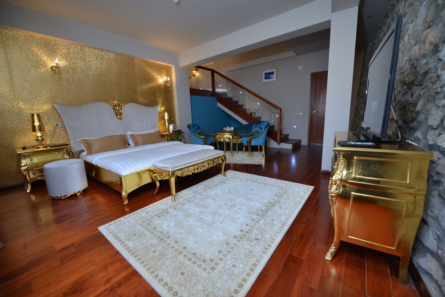 Un dormitorio con una cama grande, una pared decorada en dorado, una escalera y una silla azul.