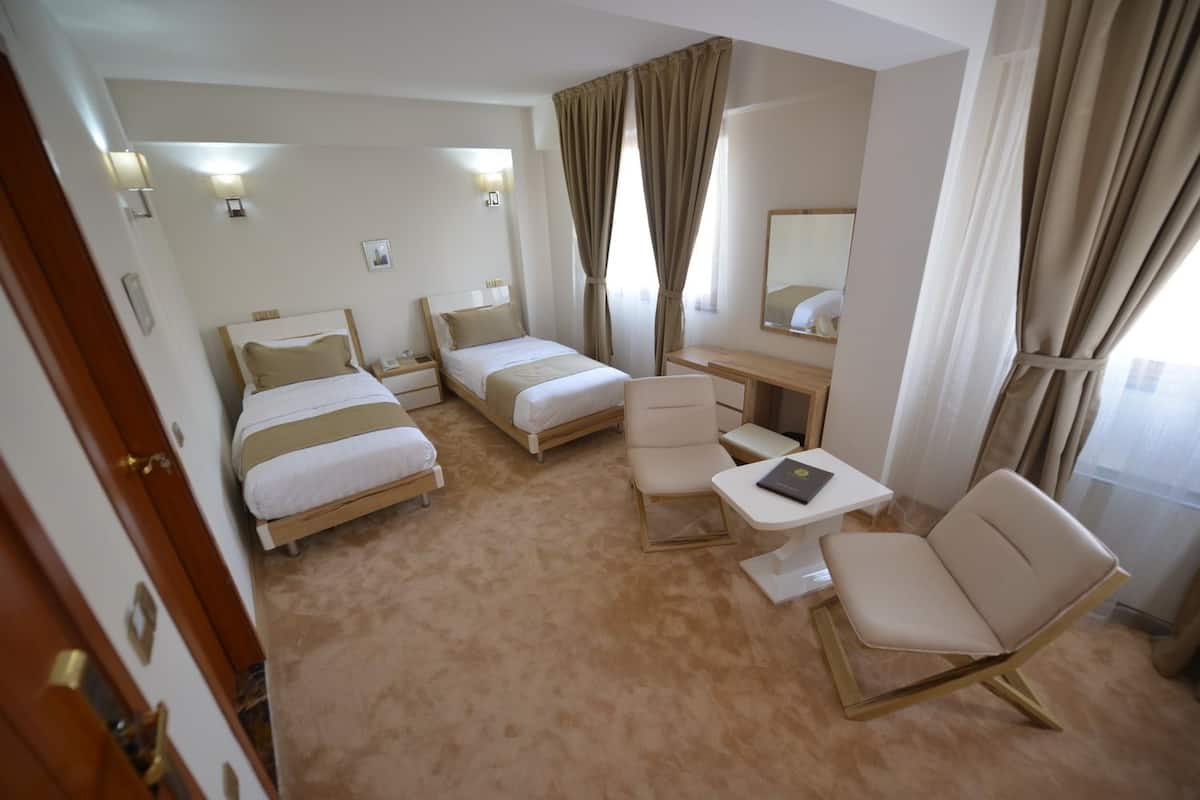 A hotel room with two single beds, a desk, a chair, and a small table.