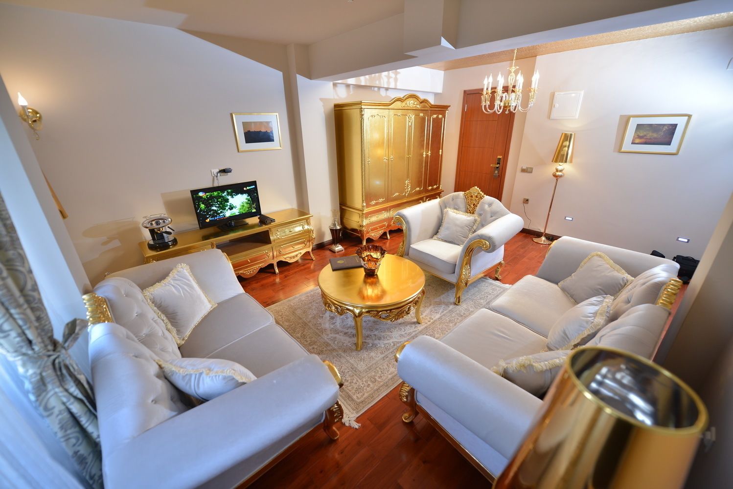 A spacious living room with a large white sofa set, a golden cabinet, and a television on a wooden stand.