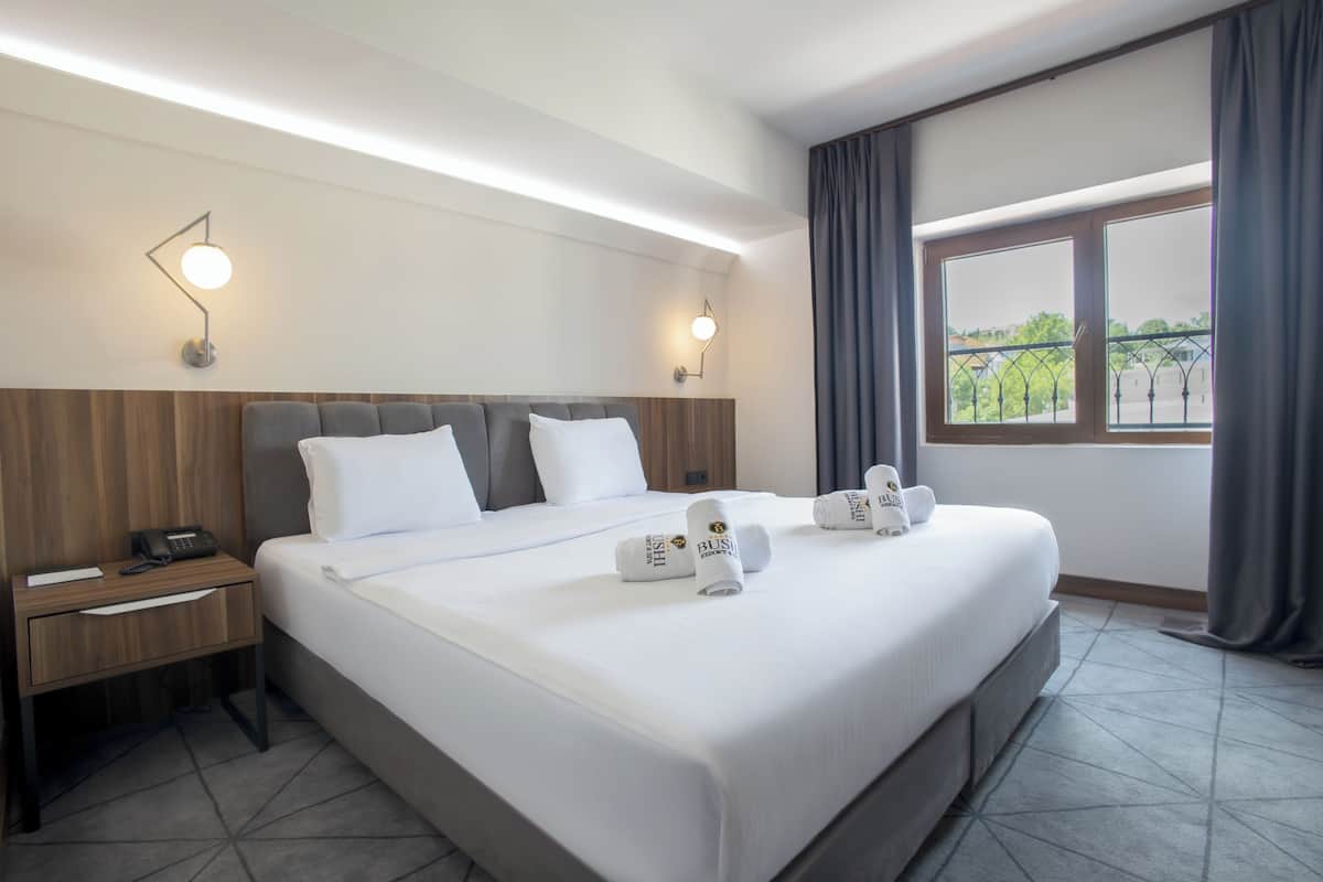 A hotel room with a large bed, two bedside tables, a telephone, and a window with curtains.