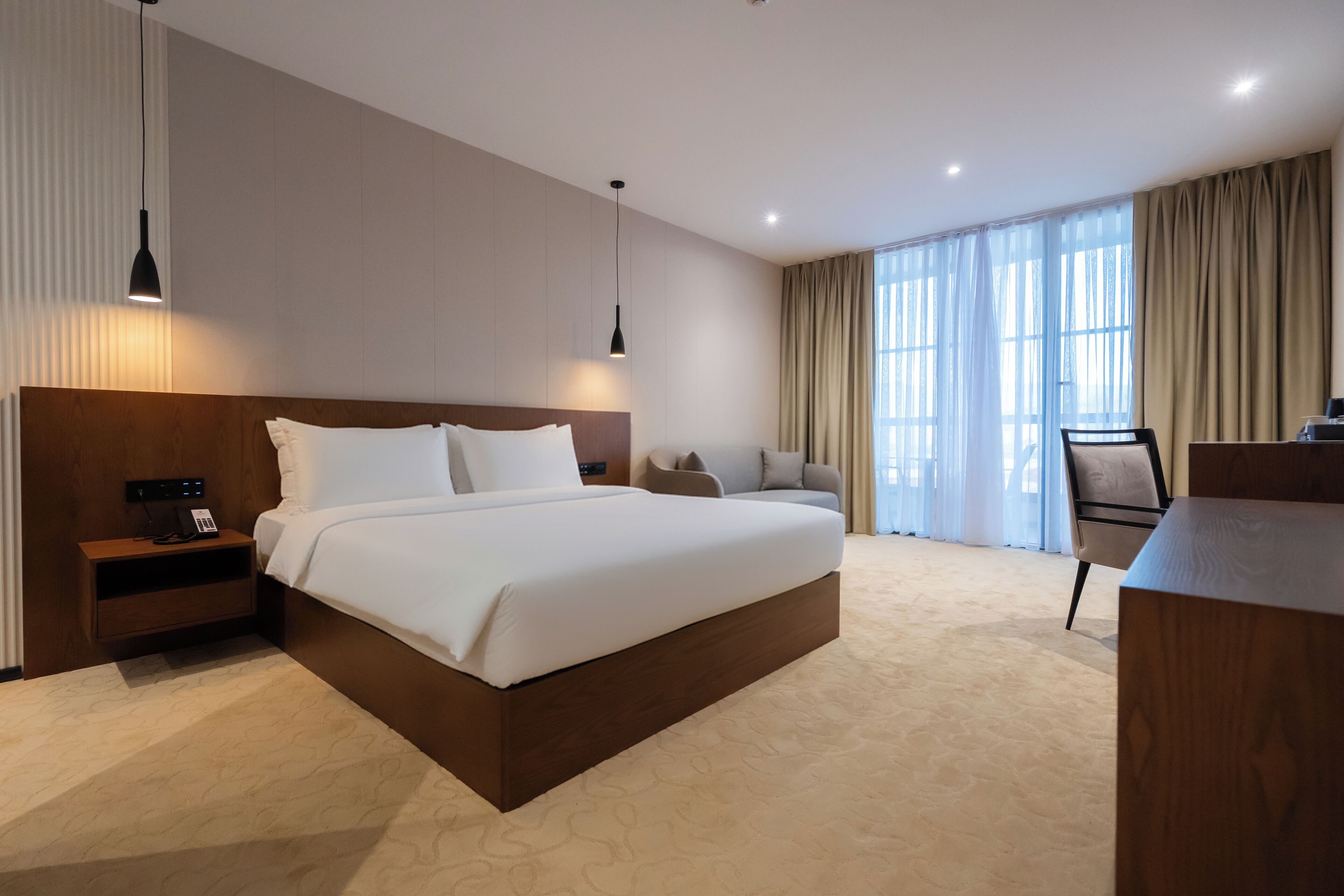 Una habitación de hotel moderna con una cama grande, mesitas de noche, un escritorio y una silla.