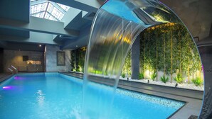 An indoor swimming pool with a clear water slide, a skylight, and a wall of greenery. - Bushi Resort & Spa (Skopje)