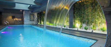An indoor swimming pool with a clear water slide, a skylight, and a wall of greenery.