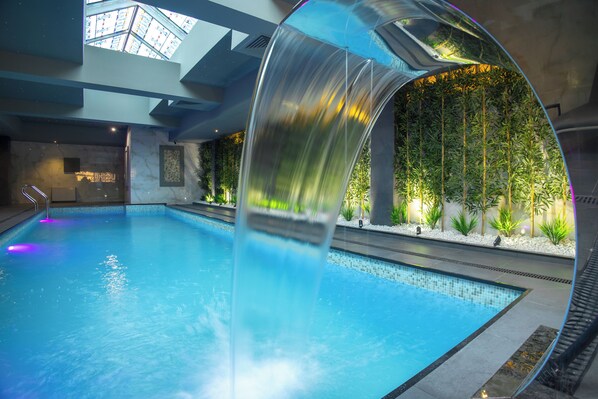 An indoor swimming pool with a clear water slide, a skylight, and a wall of greenery. - Bushi Resort & Spa (Skopje)
