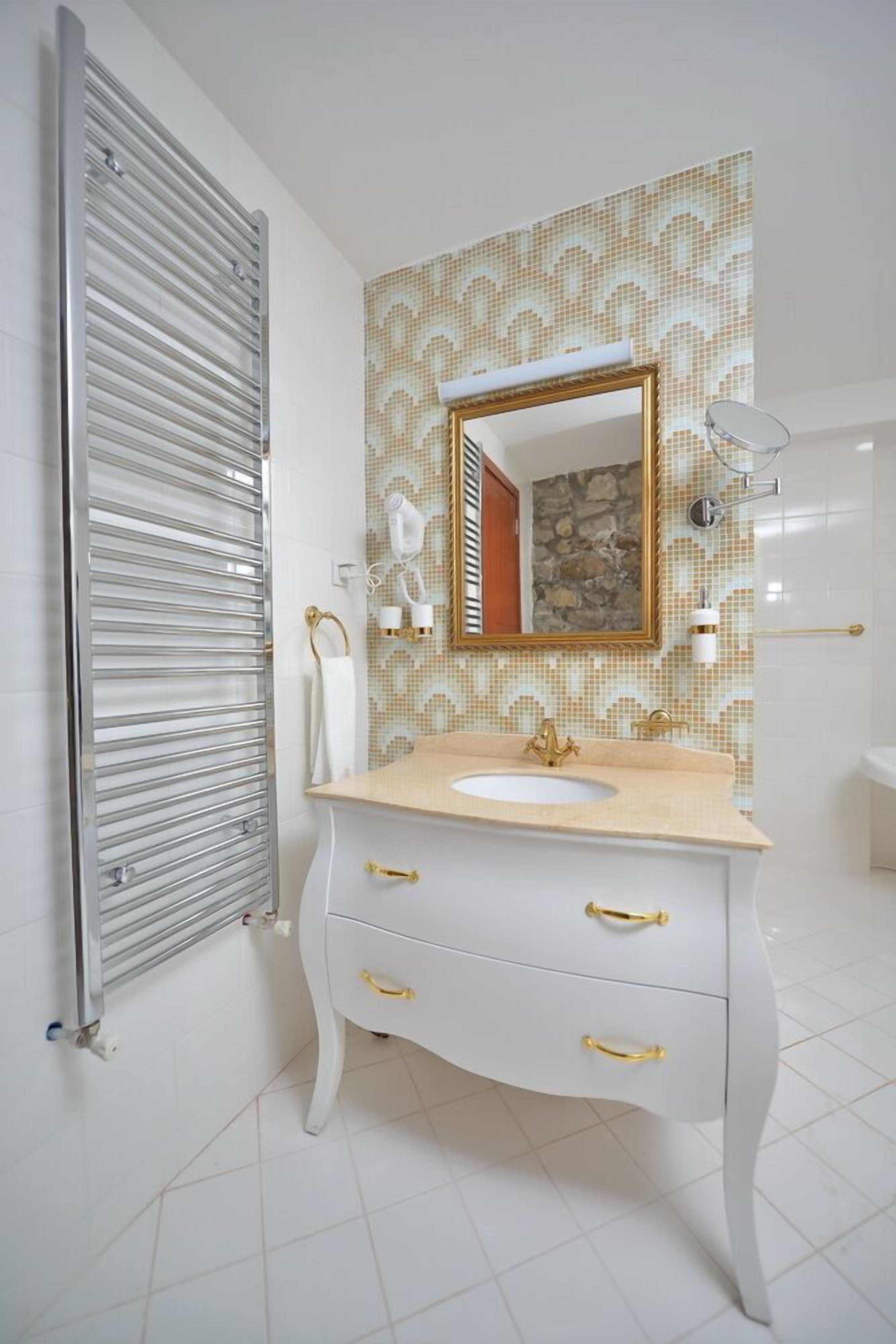Une salle de bain avec un meuble-lavabo blanc, des poignées dorées, un pare-feu décoré et un grand miroir.