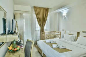 A hotel room with a bed, a desk with a computer, a chair, a crib, and a fruit bowl. - Bushi Resort & Spa (Skopje)