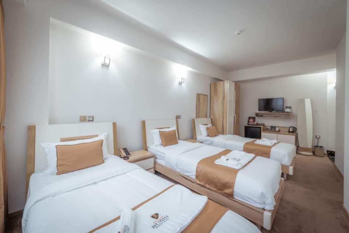 A hotel room with four single beds, a TV, a desk with a lamp, and a small seating area.