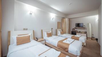 Habitación de hotel con cuatro camas individuales, un televisor, un escritorio con lámpara y una pequeña zona de estar.